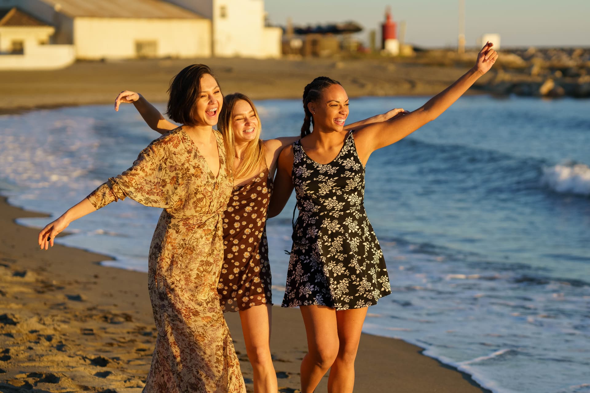 Three women walking together along the shoreline at sunset
