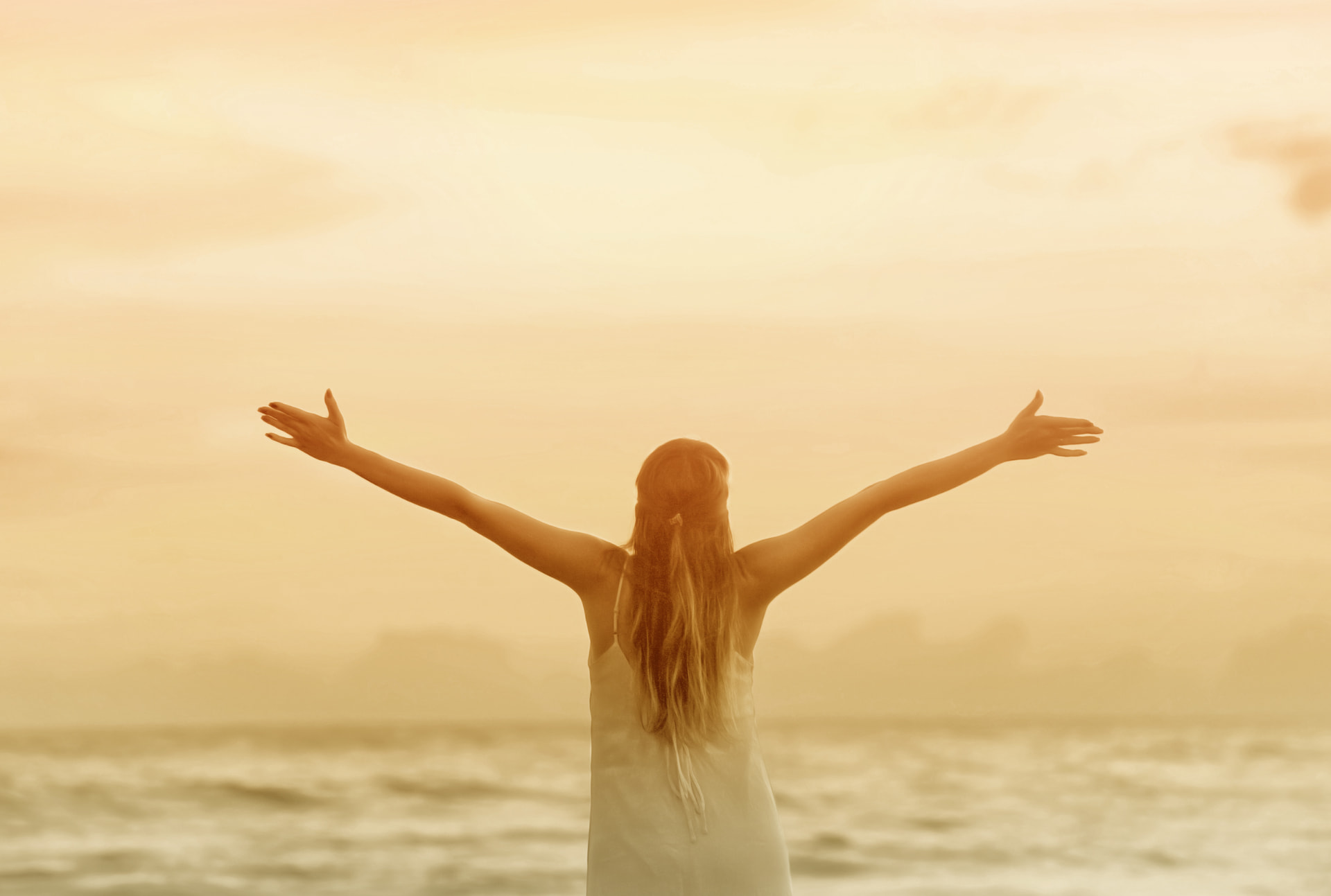 Woman with raised arms facing the sunset over the ocean